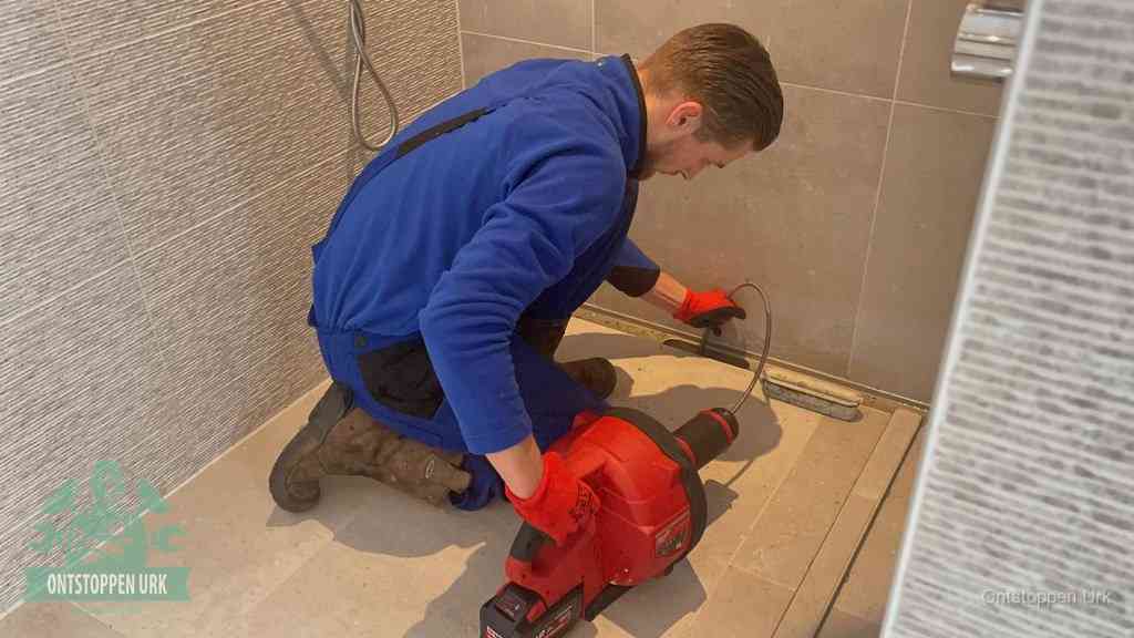 Een monteur ontstopt een langwerpige douchegoot met een elektrische veer, een doucheputje verstopt door haren en zeep in Urk