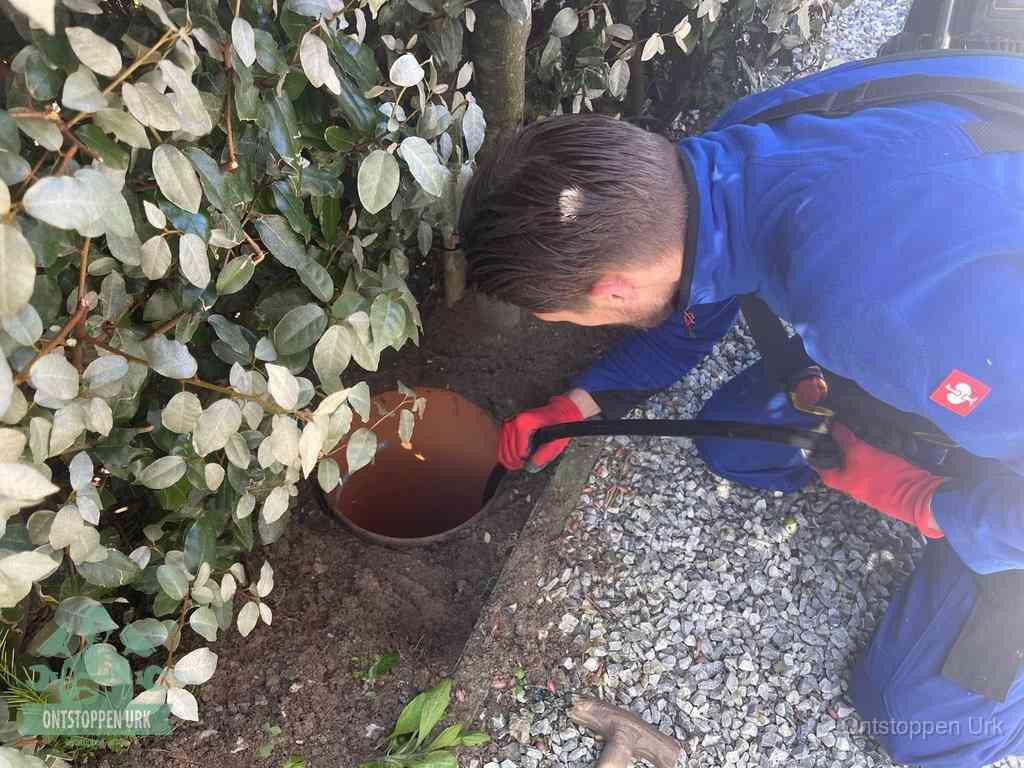 Een monteur voert een slang in een geopende rioolput in de tuin om het hoofdriool te ontstoppen in Urk