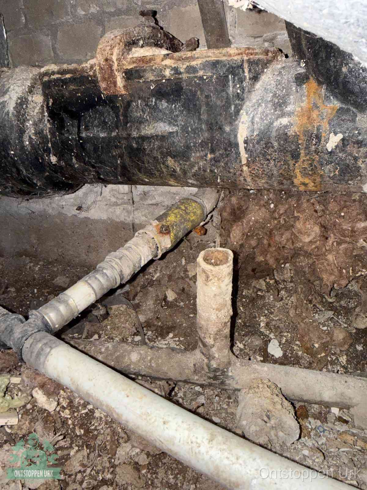 Een oude hoofdrioolbuis met roest- en kalkaanslag in een kruipruimte, oorzaak van terugkerende structurele rioolproblemen in Urk